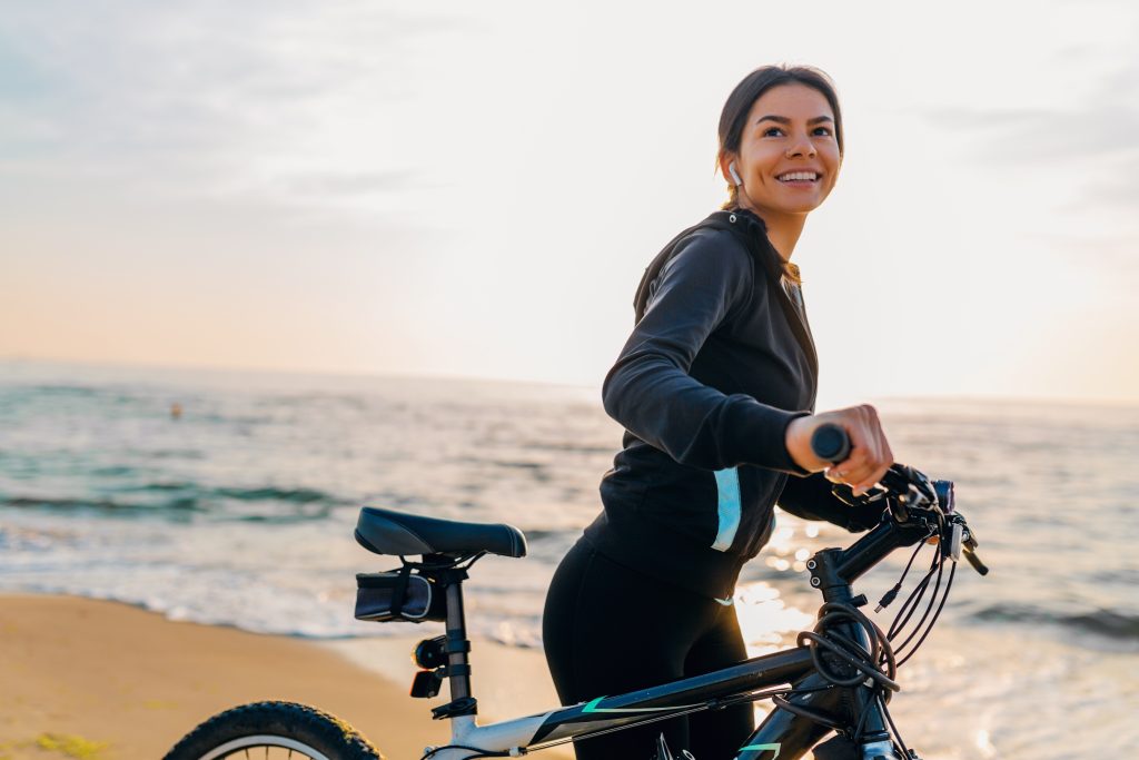 Imagen de una mujer en bicicleta con fondo de una playa.